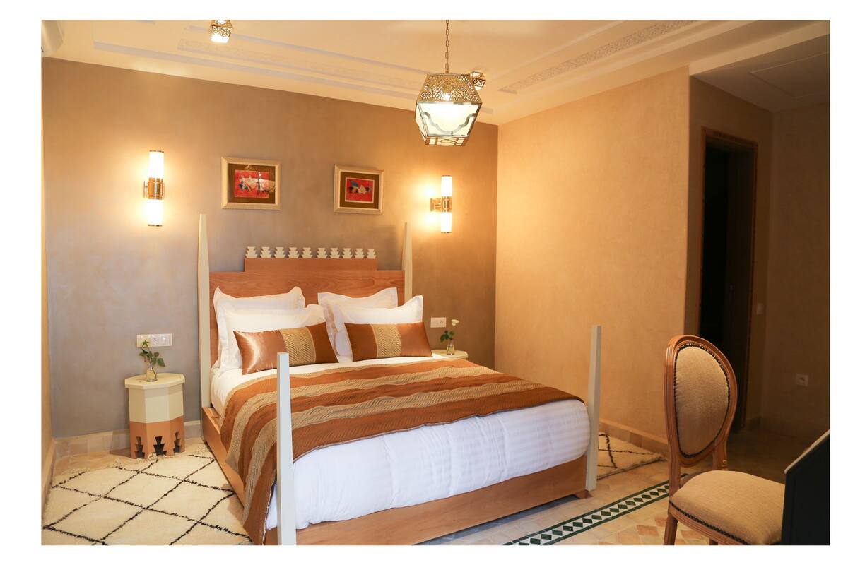 A bedroom with a large bed, bedside tables, a chair, and wall-mounted lights.