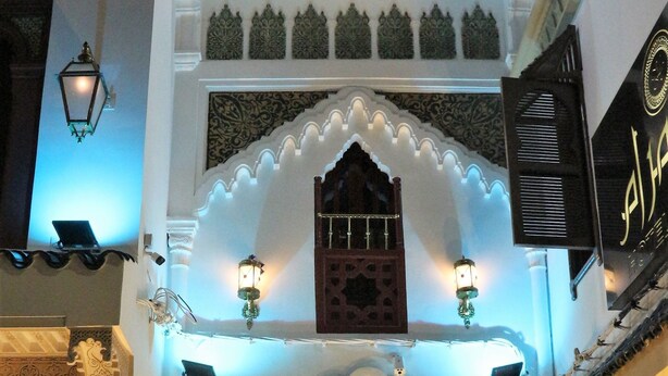 A traditional Moroccan architectural entrance with ornate carvings, a wooden door, and a small window above it. - Palais Zahia (Tangier)