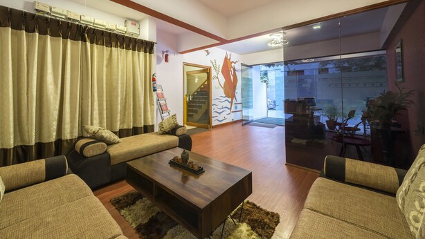 A living room with sofas, a coffee table, and a glass door leading to a balcony. - Hotel Raj Comforts - Golf View (Bengaluru)