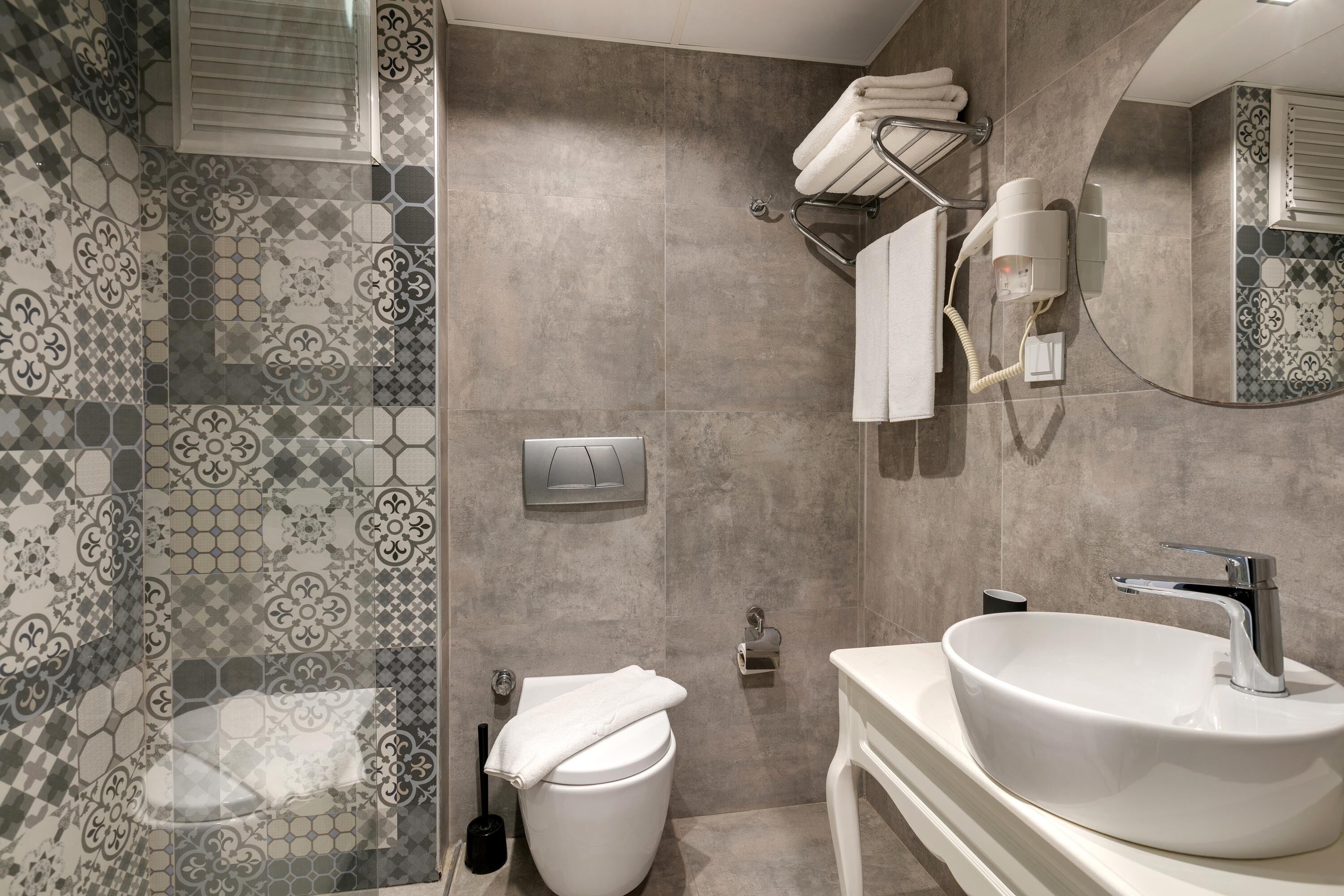 A bathroom with a white sink, a toilet, and a shower area with patterned tiles.