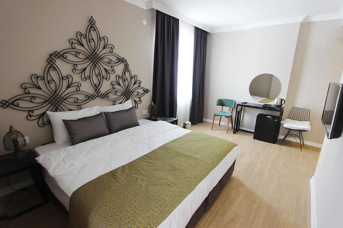 A hotel room with a large bed, a desk with a mirror, a chair, and a TV.