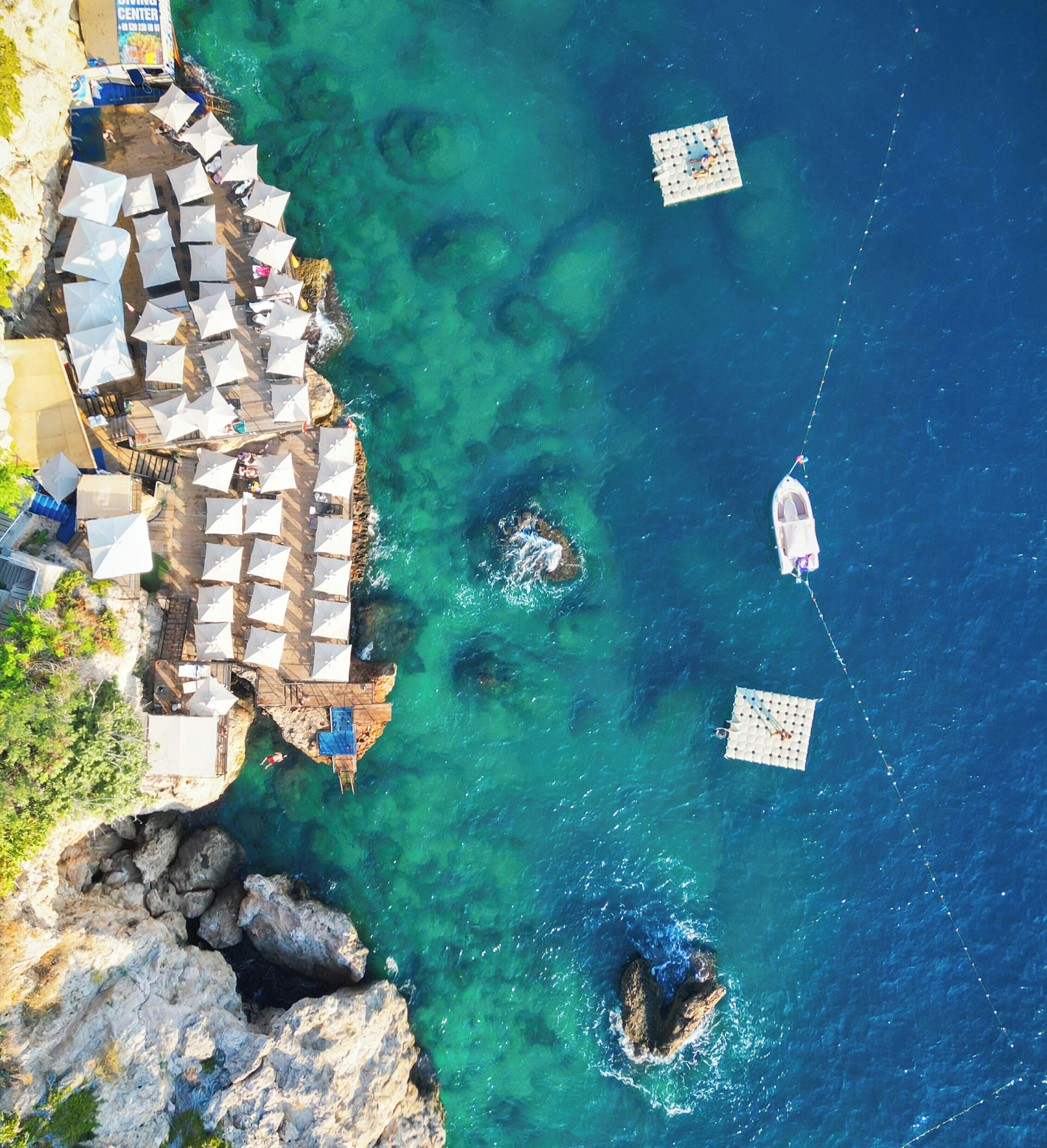An aerial view of a coastal area with a beach, umbrellas, and a boat.
