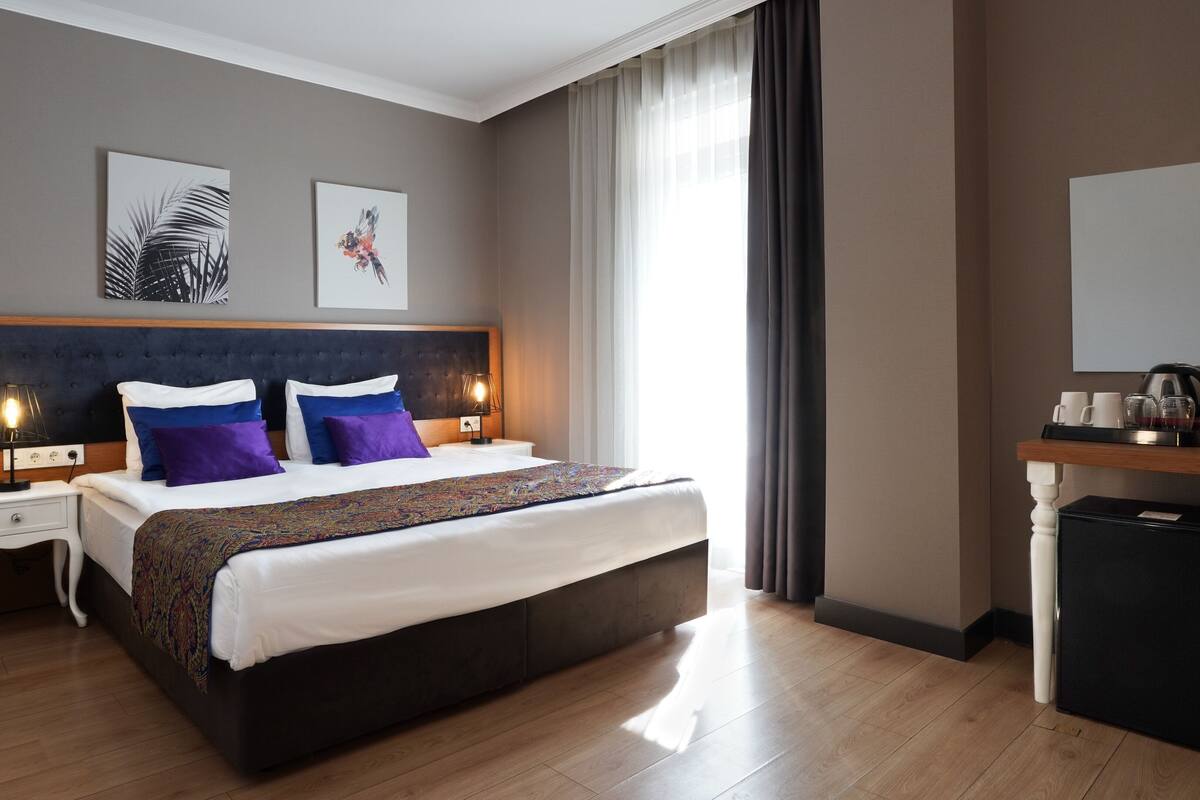 A hotel room with a large bed, bedside tables, a desk, a coffee machine, and artwork on the walls.