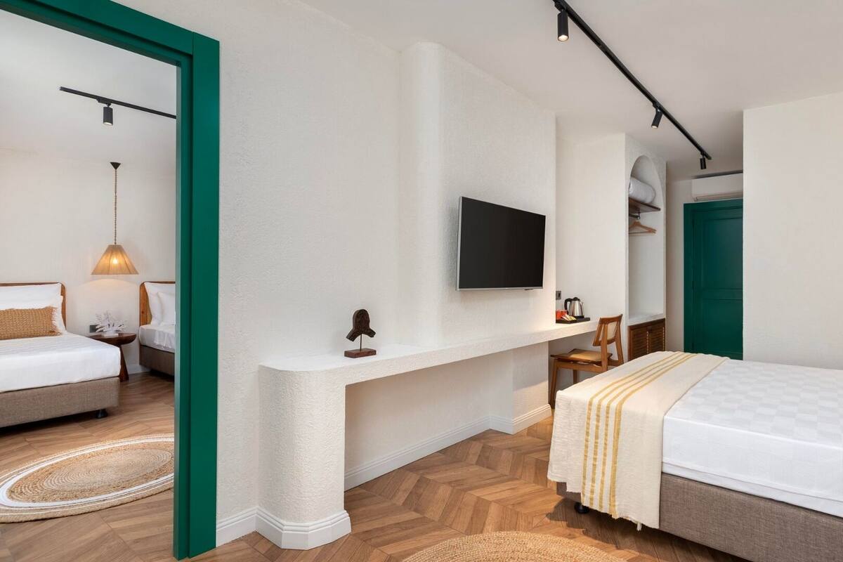 A modern hotel room with a large bed, a desk with a flat-screen TV, and a green-framed mirror.