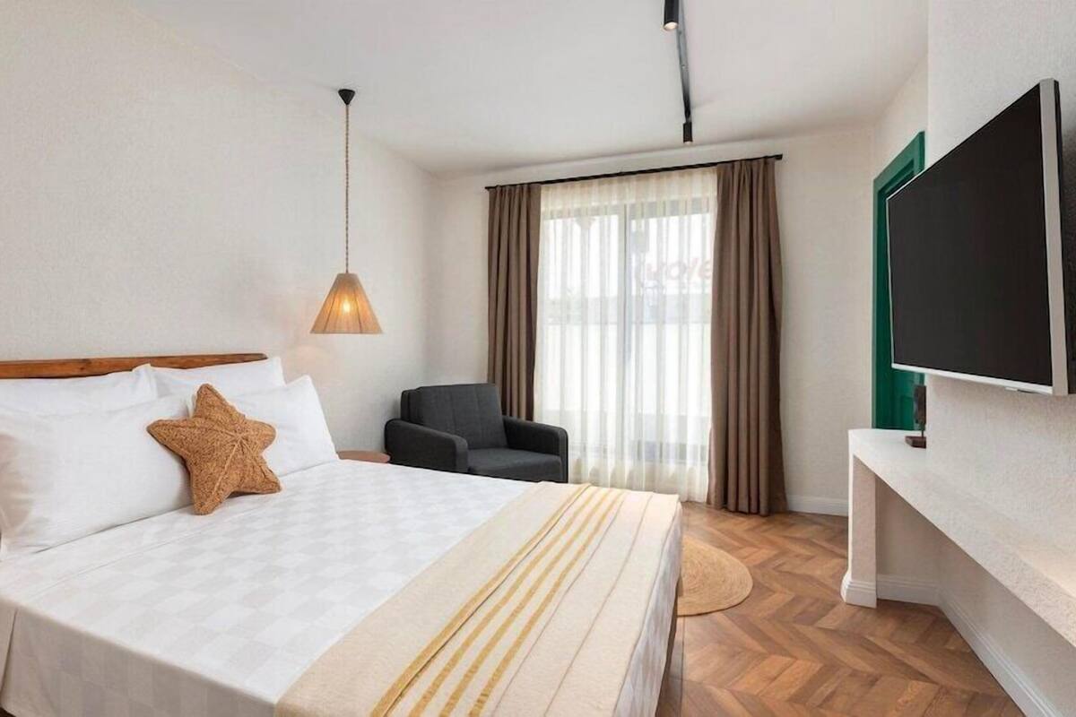 A hotel room with a bed, a chair, a TV, and a window with curtains.