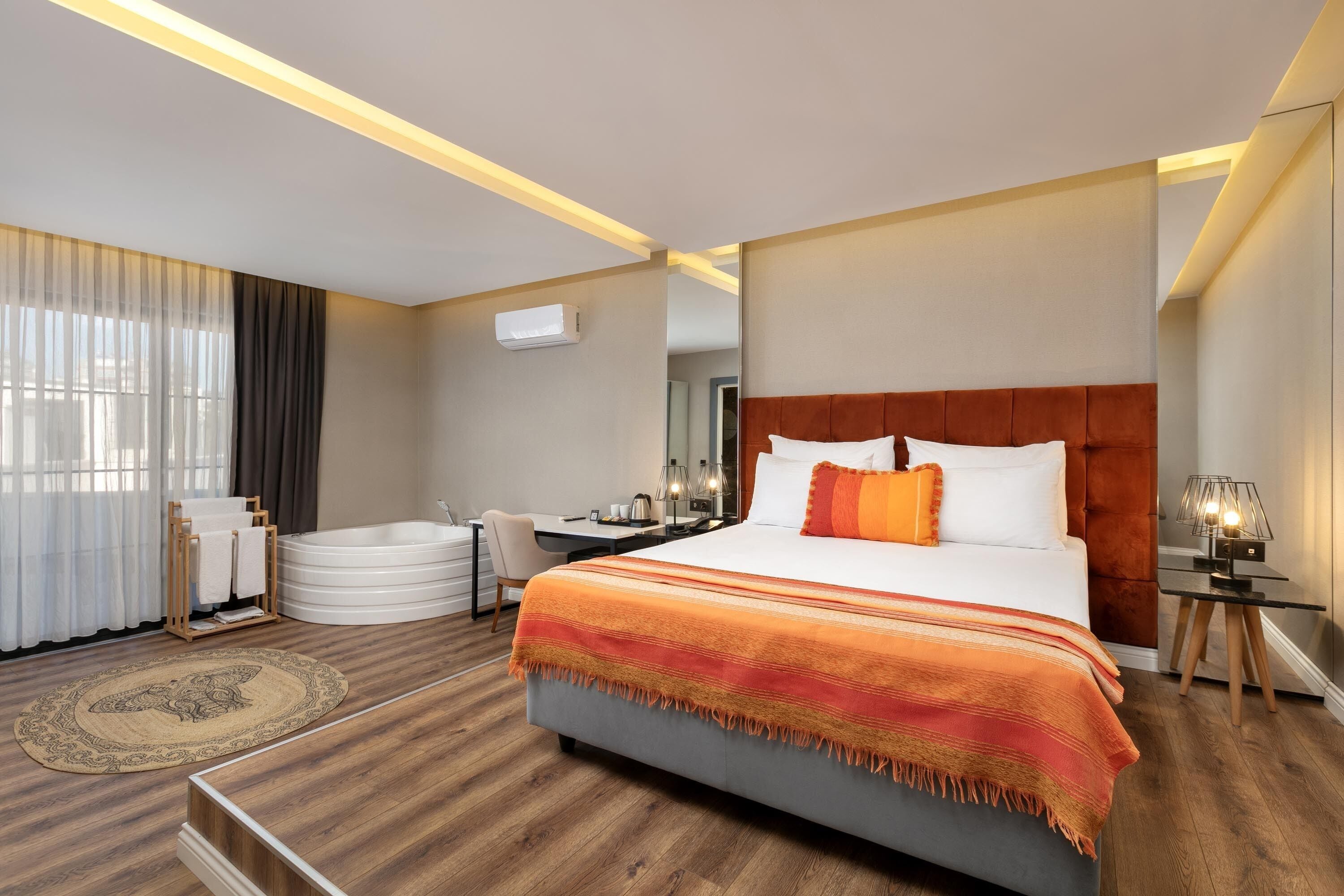 Een moderne hotelkamer met een groot bed, een bureau, een stoel, een badkuip en een groot raam met gordijnen.