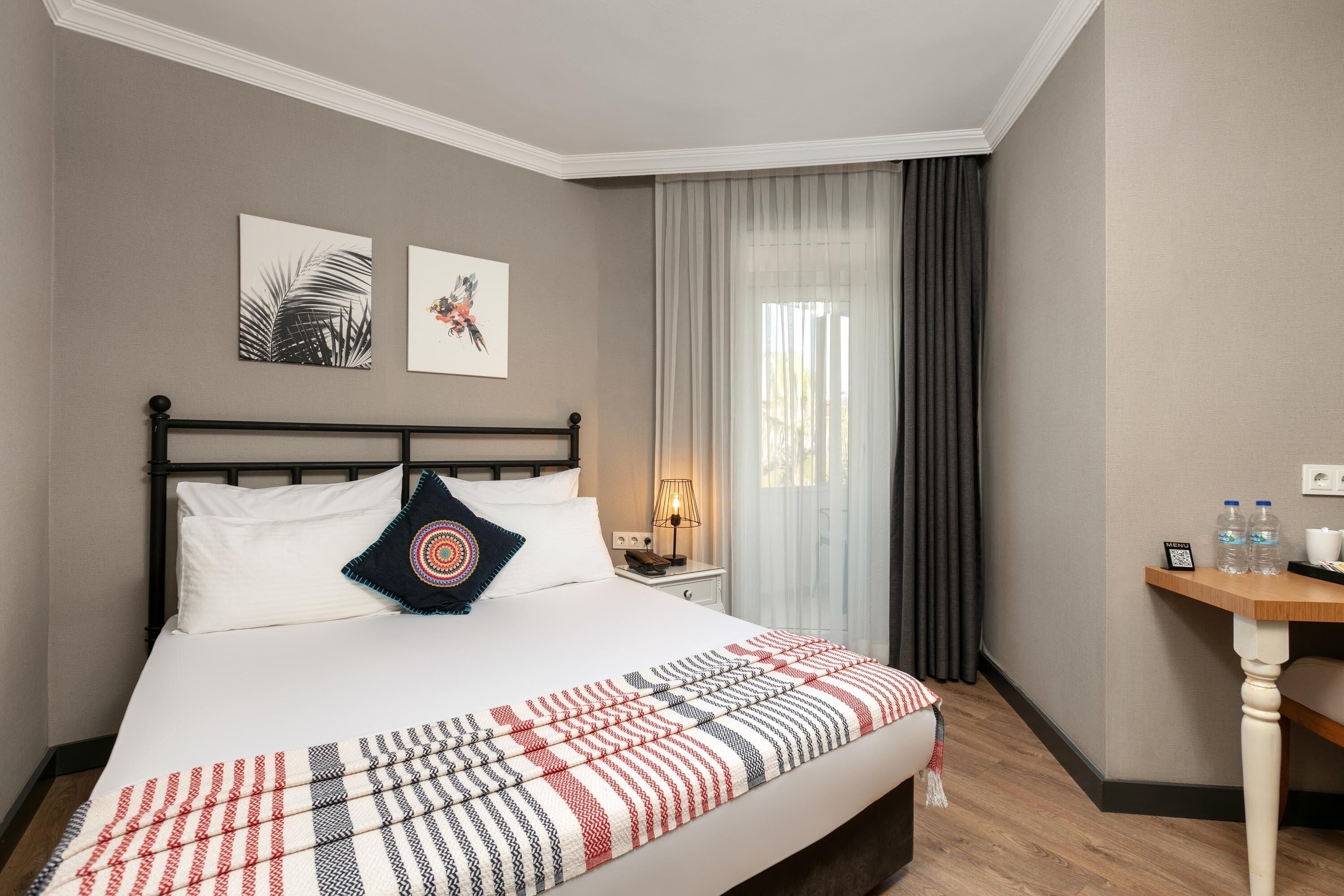 Een hotelkamer met een bed, nachtkastje, bureau en raam met gordijnen.