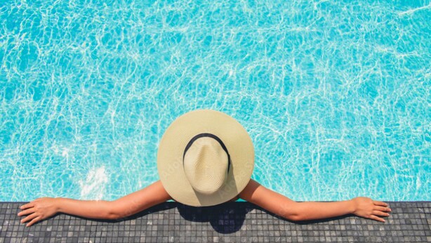 Une personne allongée au bord d’une piscine, les bras tendus, portant un chapeau, et une piscine avec une eau d’un bleu limpide.