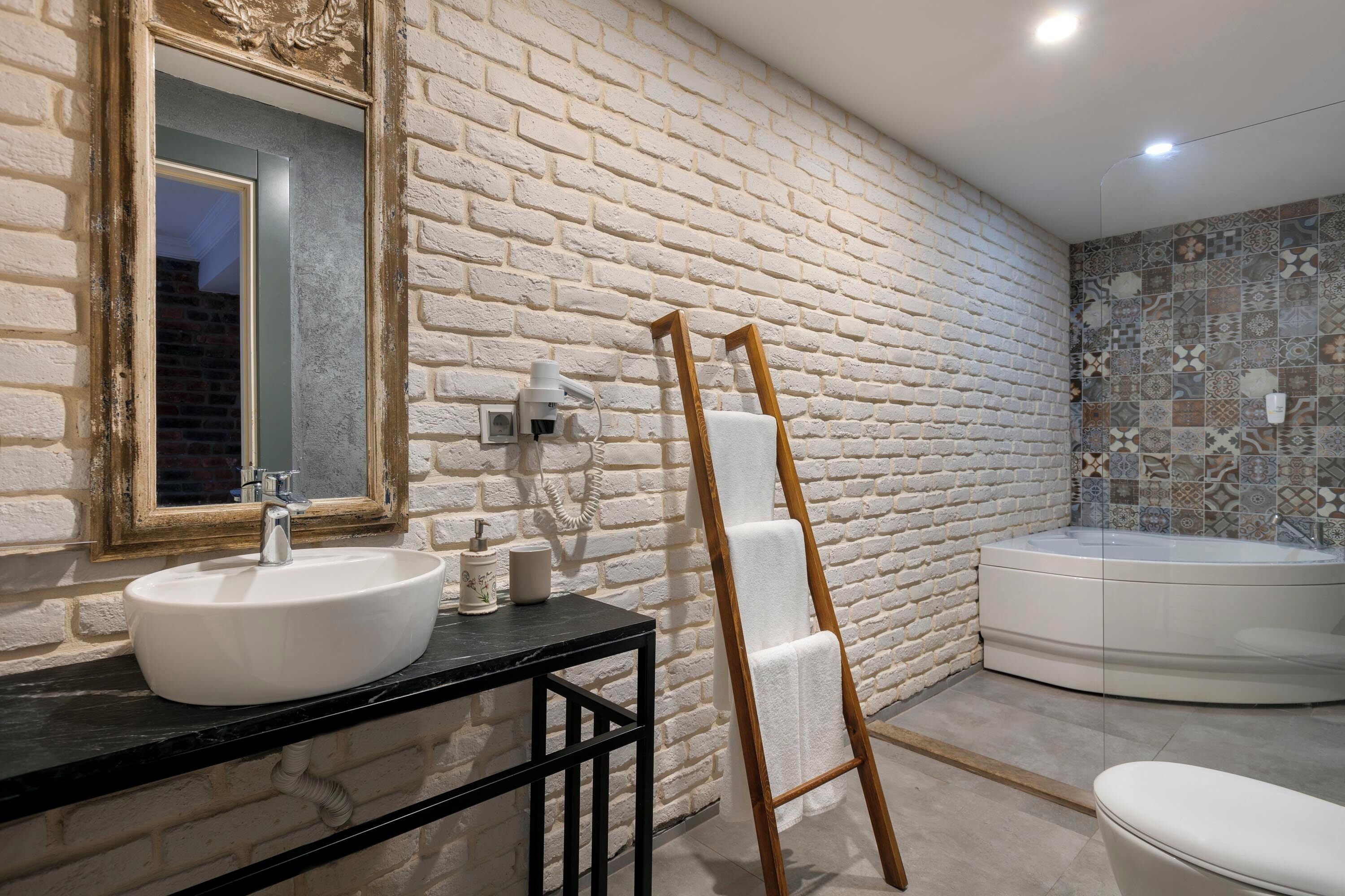 Une salle de bain avec un lavabo blanc, une échelle en bois, une baignoire et un mur carrelé.