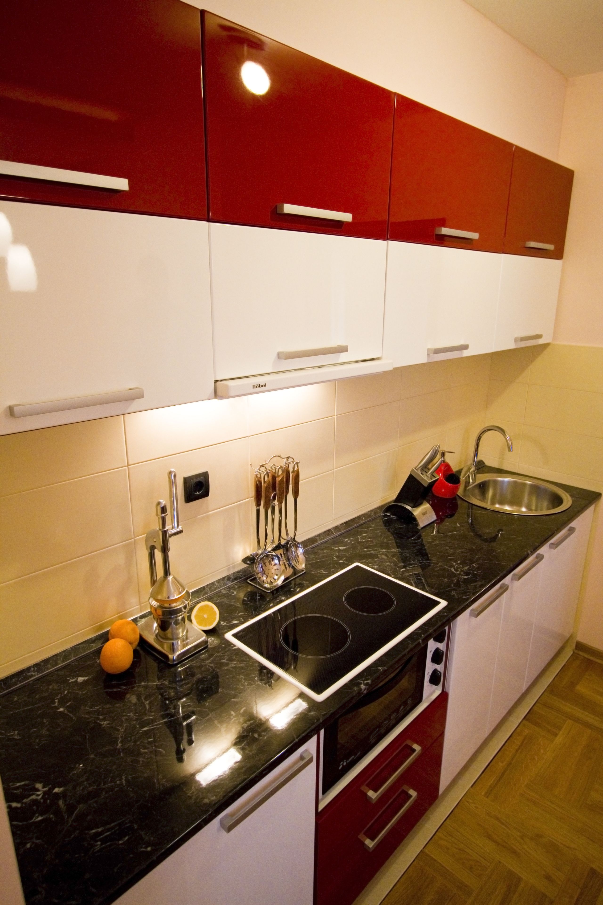 A modern kitchen with red and white cabinets, a black countertop, and stainless steel appliances.