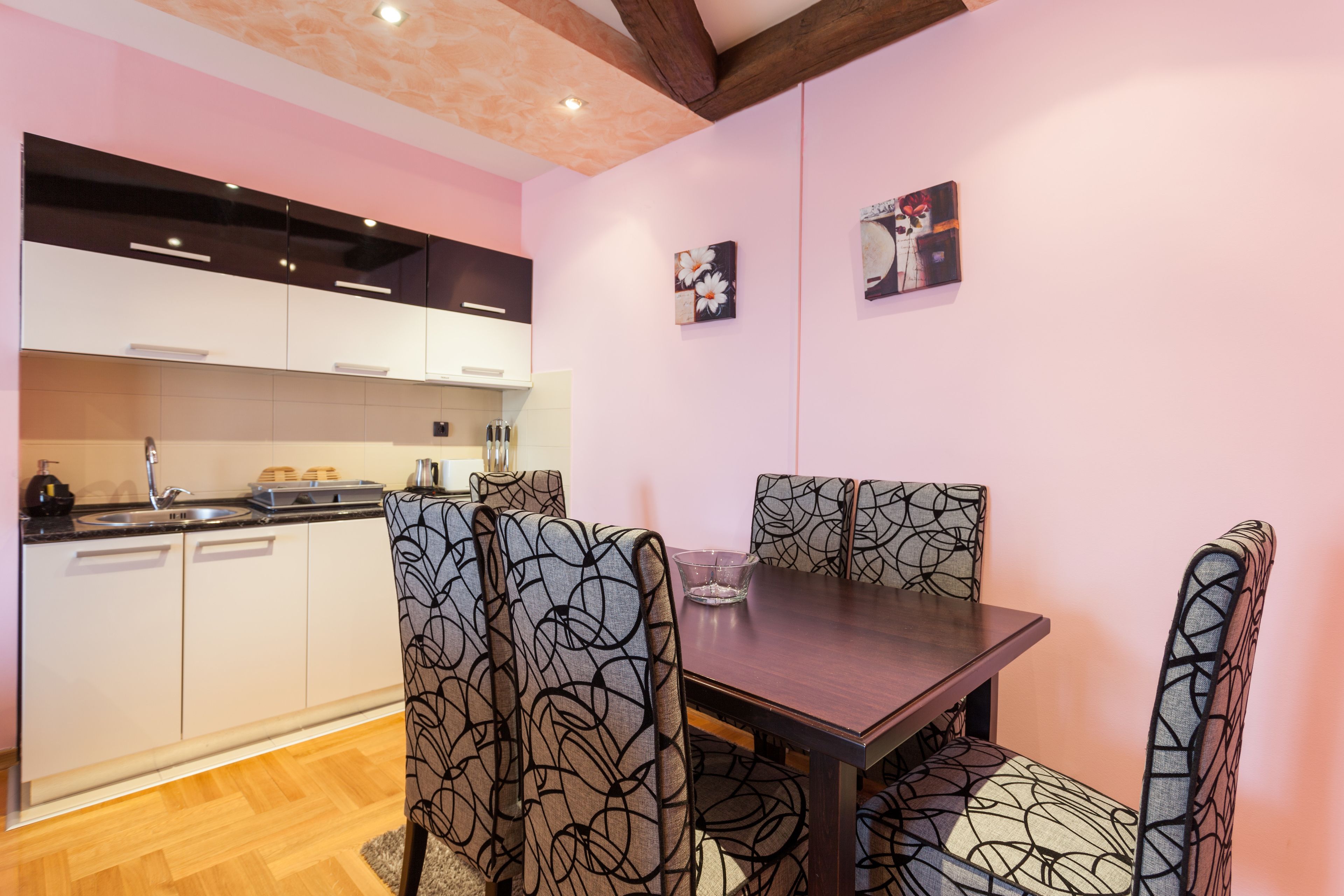 Cocina moderna con armarios blancos, encimera de madera y comedor con sillas estampadas y una mesa de madera oscura.