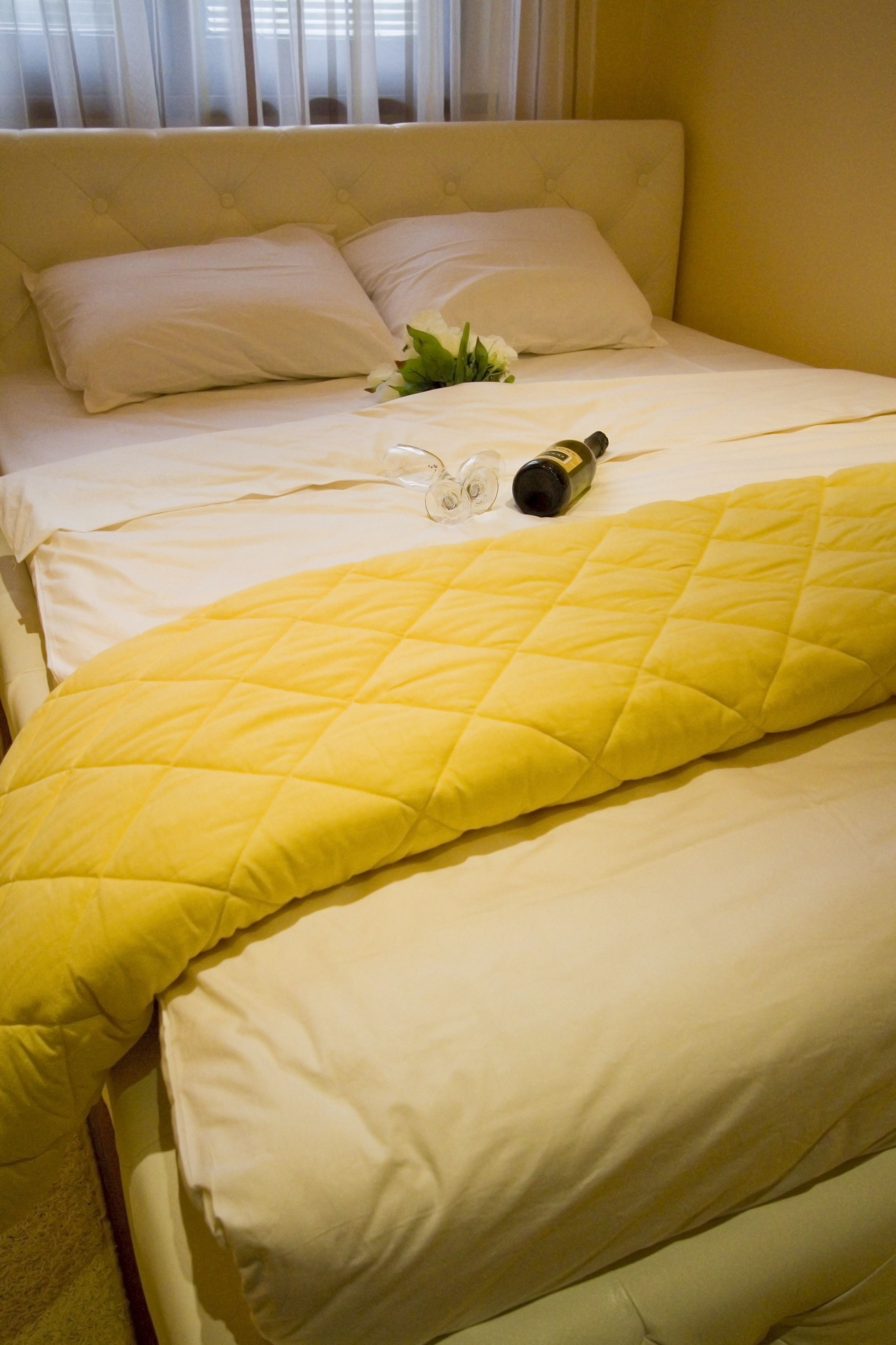 A bed with a yellow quilt, white pillows, and a bottle of champagne.