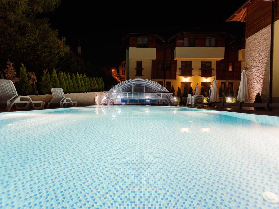 Une piscine entourée de bâtiments dont les fenêtres sont illuminées, avec des chaises longues et des parasols à proximité.