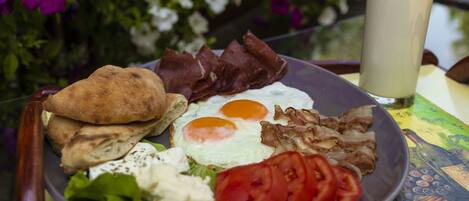A plate of breakfast with eggs, bacon, tomatoes, lettuce, and bread on a table with a glass of milk.