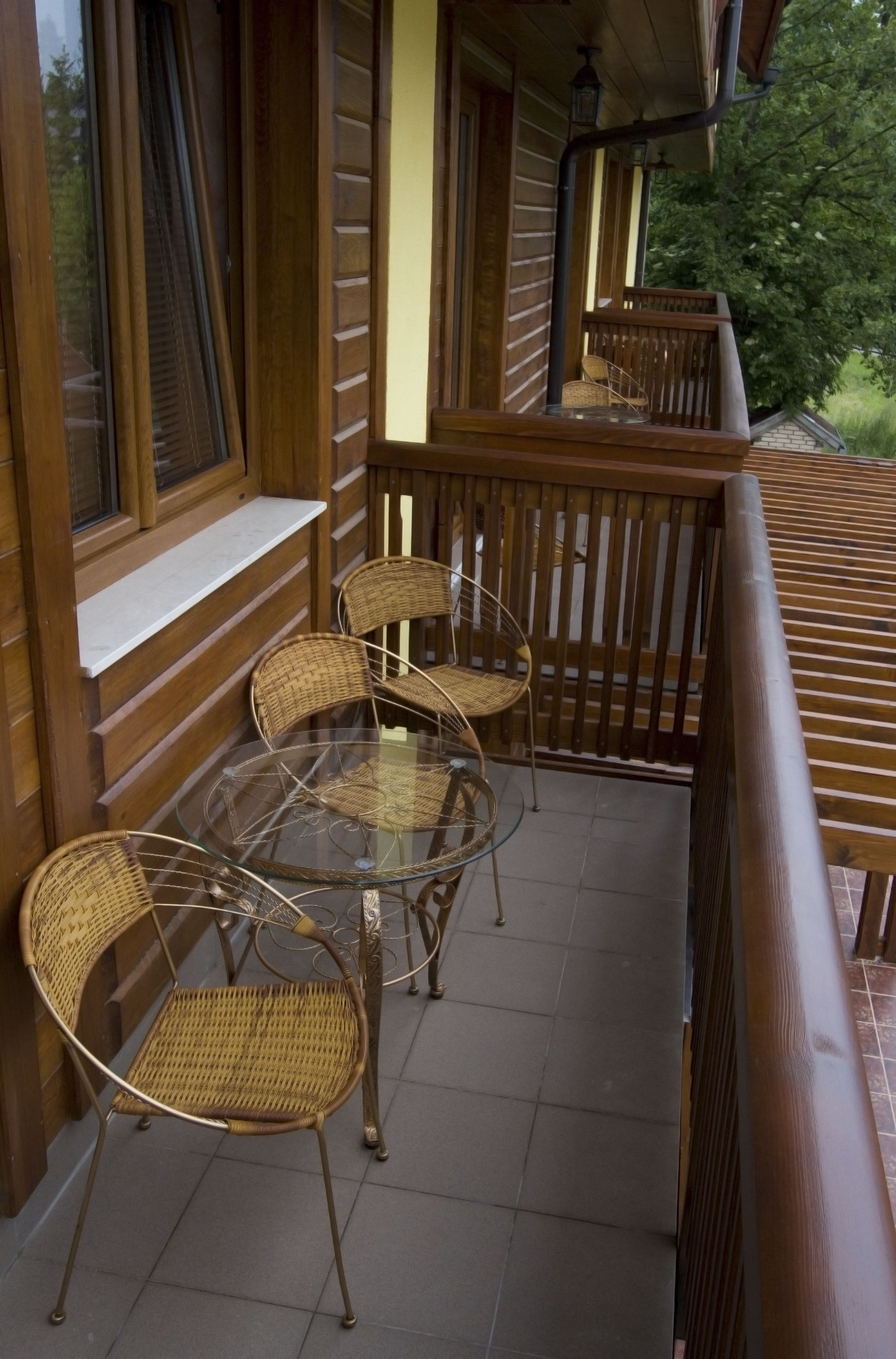 A wooden balcony with wicker chairs and a glass table.