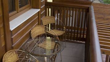 A wooden balcony with wicker chairs and a glass table.