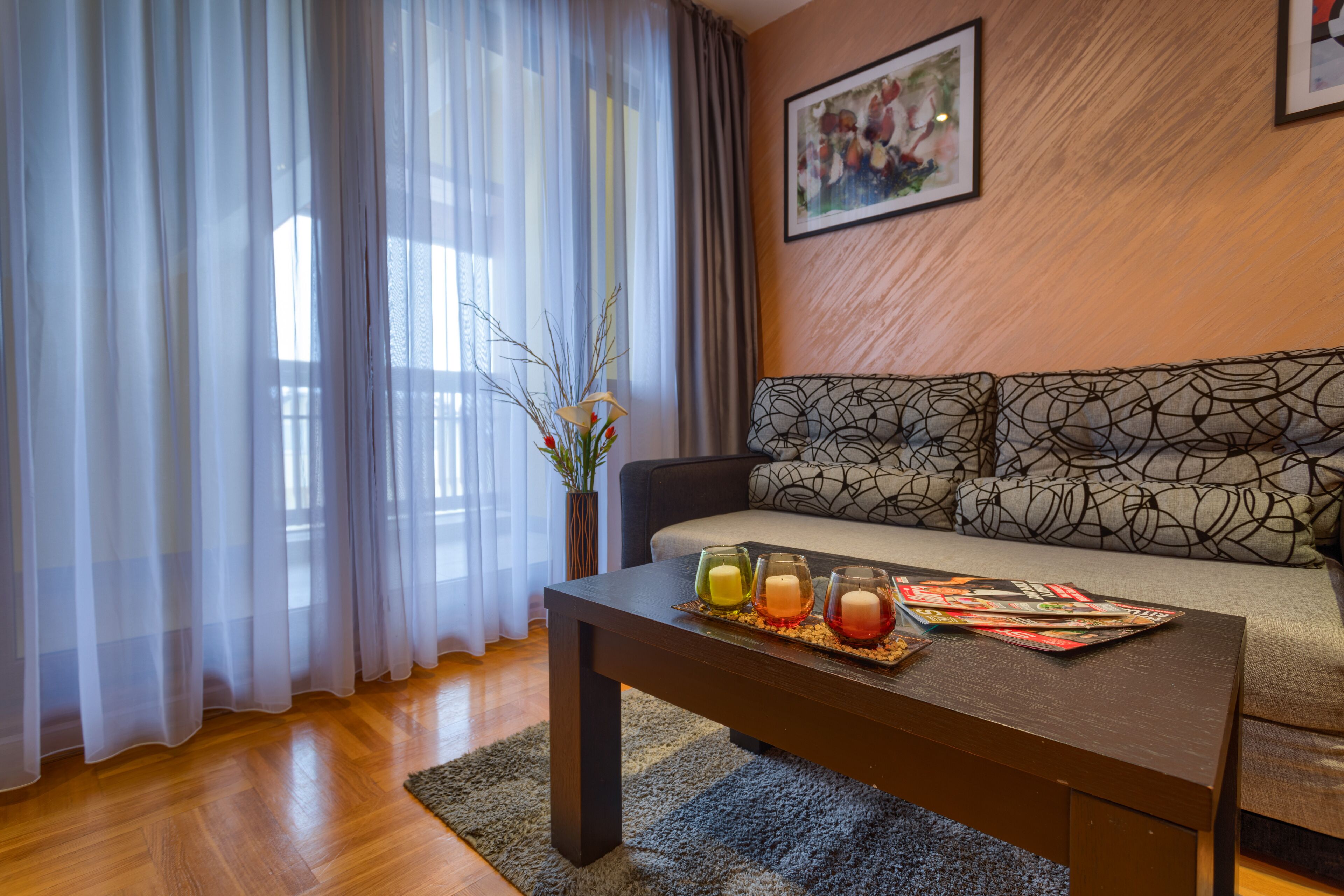 A modern living room with a sofa, a coffee table with candles, and a vase with branches.