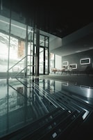 Un área de piscina interior moderna con barandillas de cristal, sillones de descanso y vistas despejadas al exterior.