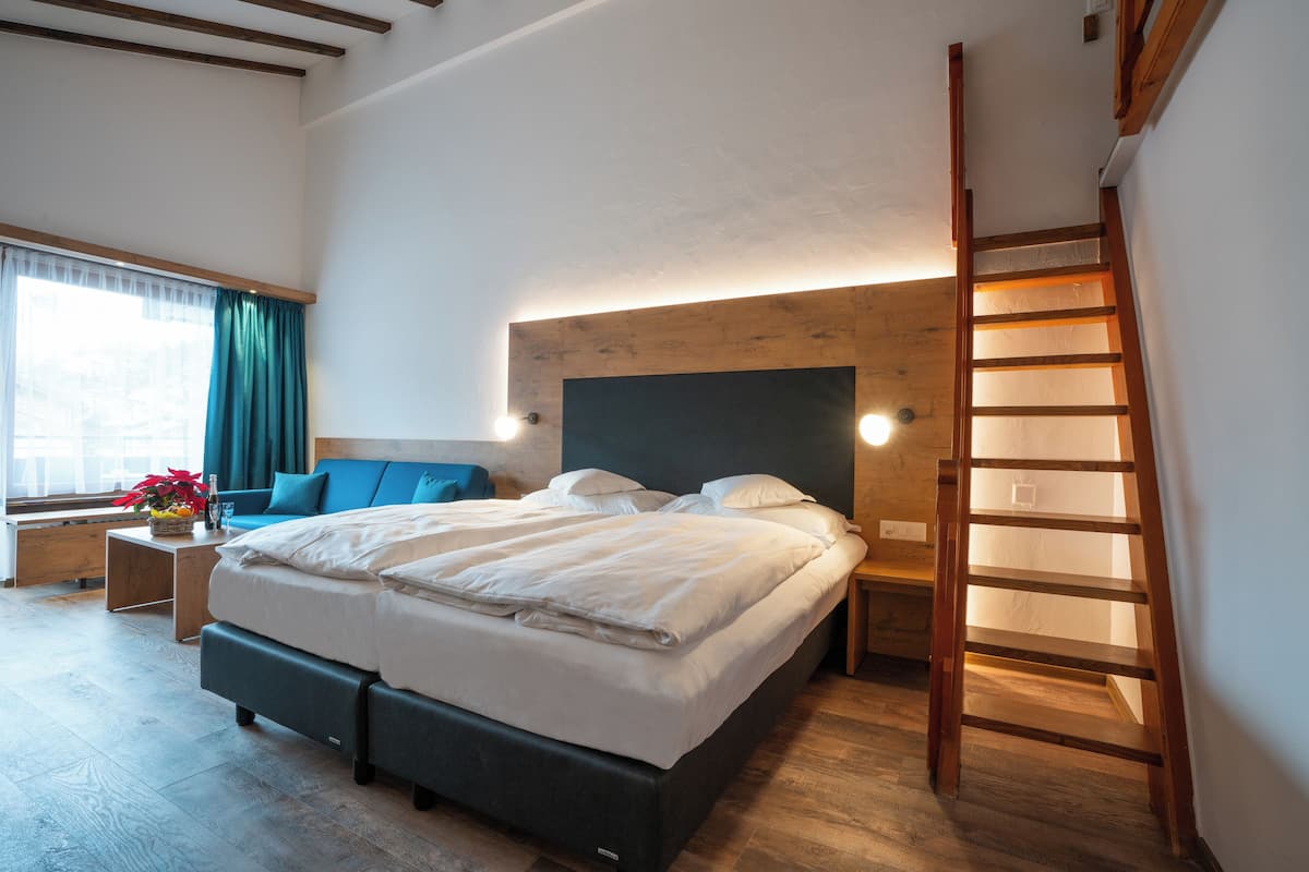 A modern bedroom with a large bed, a wooden headboard, a bedside table, a nightstand, a window with curtains, and a wooden ladder.