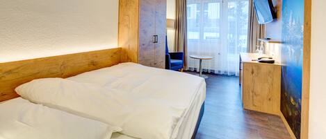 A hotel room with a large bed, a desk with a chair, a television mounted on the wall, and a window with curtains.