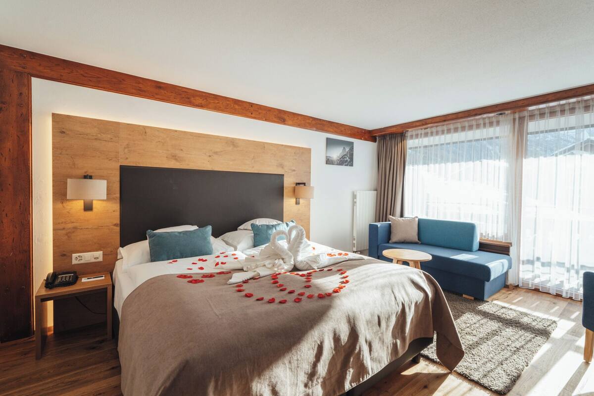 A modern hotel room with a large bed, a blue sofa, and a small table.