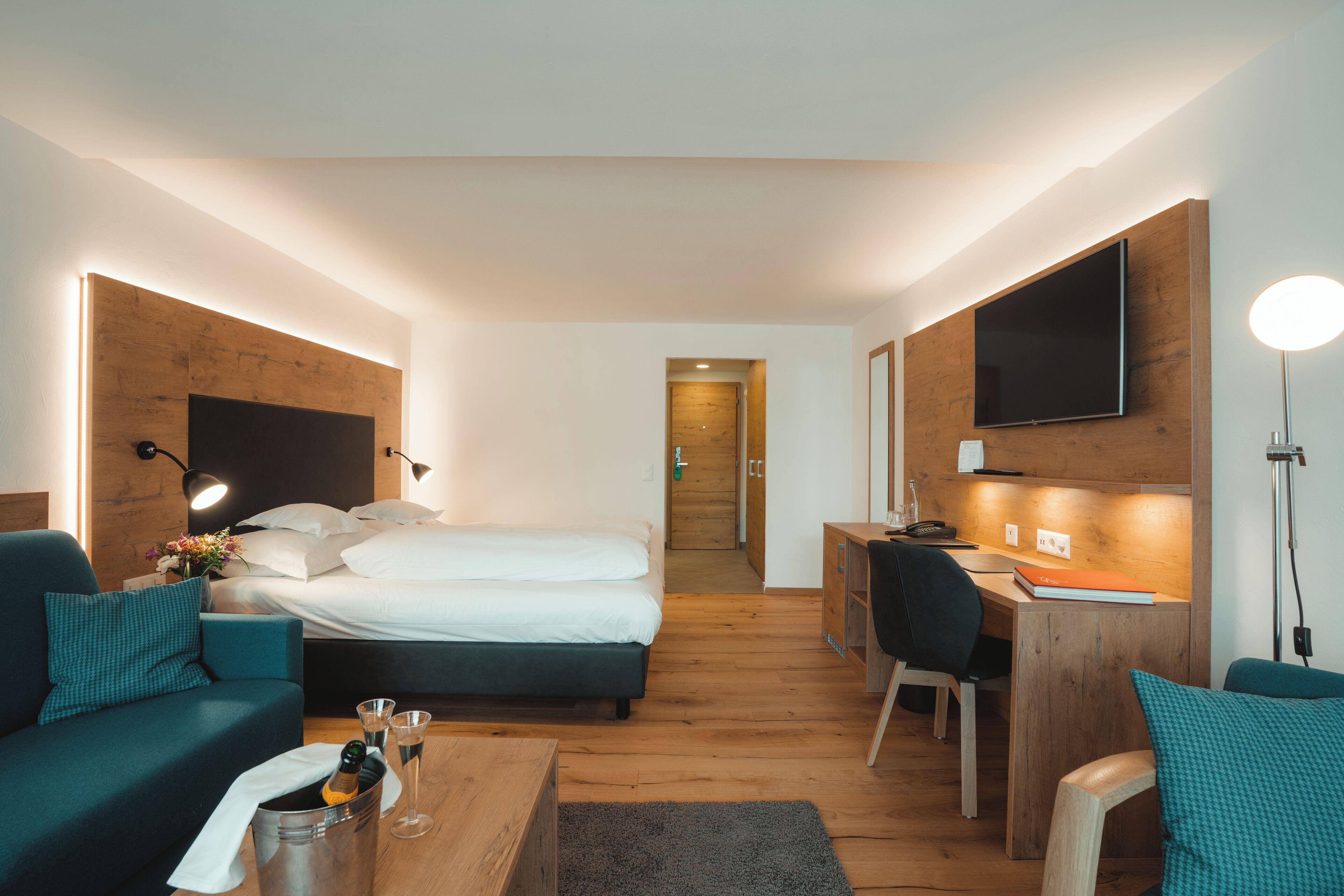 Habitació d'hotel amb un llit, una taula de treball, una cadira, una taula de cafè amb begudes i una televisió penjada a la paret.