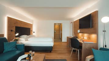 Una camera d'albergo con un letto, una scrivania, una sedia, un tavolino con bevande e un televisore a parete.