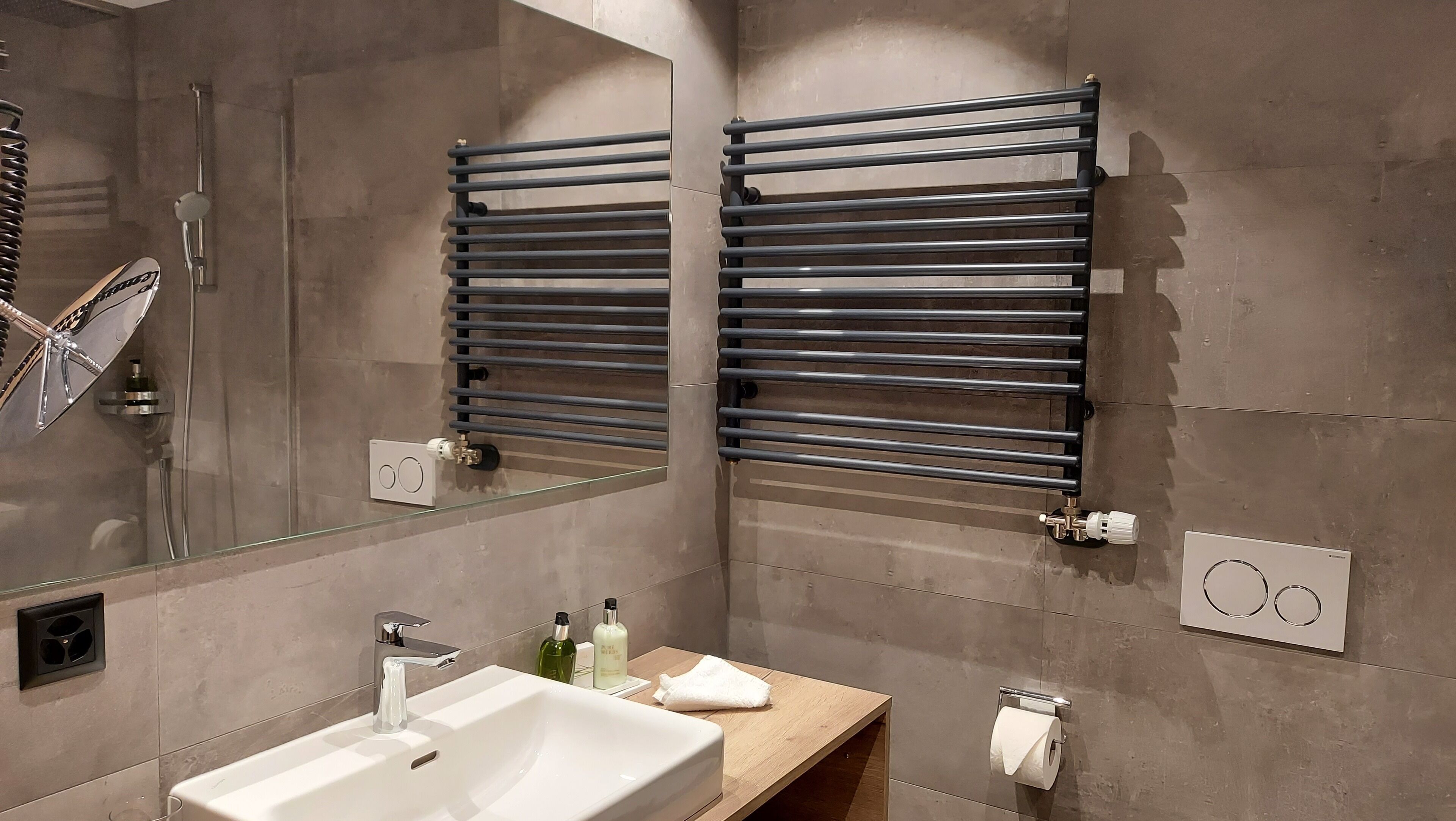 A modern bathroom with a large mirror, a white sink, a towel rack, and a shower.