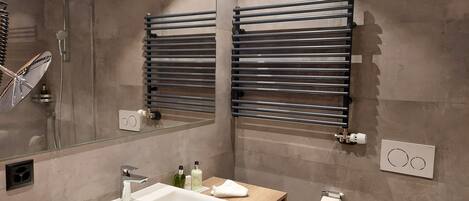A modern bathroom with a large mirror, a white sink, a towel rack, and a shower.
