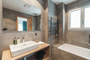 Un baño moderno con un espejo grande, un lavabo, un perchero para toallas y una bañera.
