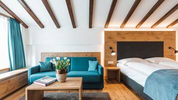 A modern bedroom with a wooden ceiling, a teal sofa, a wooden bedside table, a bed with a blue blanket, and a nightstand with a lamp.