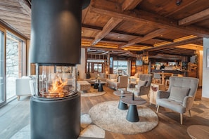 A cozy lounge area with a wood-burning stove, comfortable seating, and a stone wall.