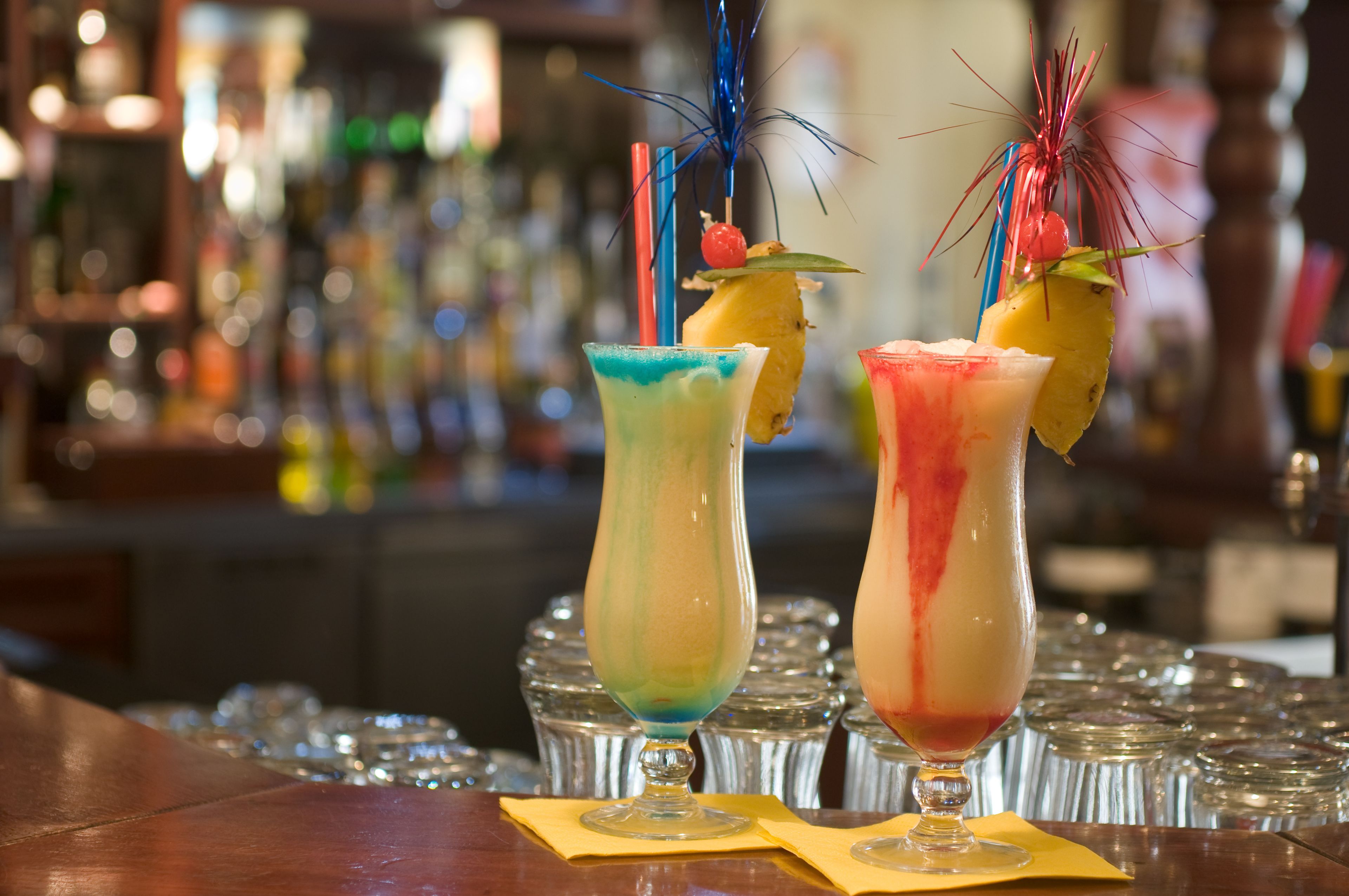 Two colorful cocktails with decorative skewers on a bar counter.