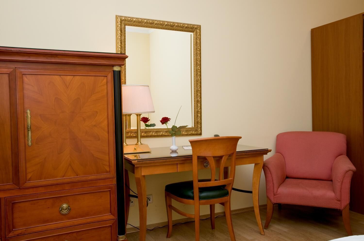 Quarto com guarda-roupa de madeira, escrivaninha com luminária, cadeira e poltrona rosa.