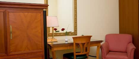 Una habitación con un armario de madera, un escritorio con una lámpara, una silla y un sillón rosa.
