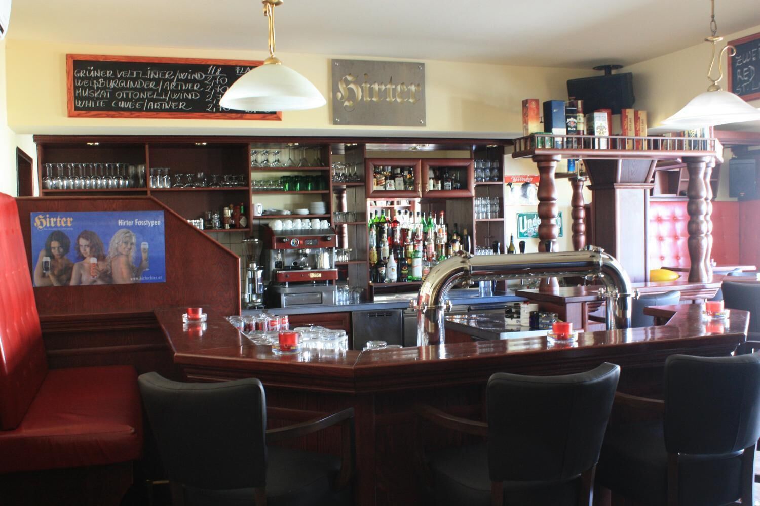 Un área de bar con mobiliario de madera, estantes con botellas y un menú en una pizarra.