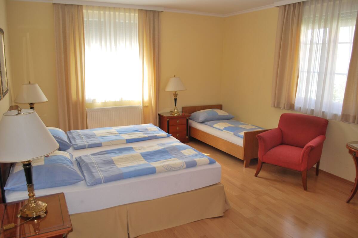 A hotel room with two beds, a red armchair, and two bedside tables with lamps.