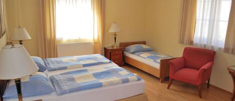 A hotel room with two beds, a red armchair, and two bedside tables with lamps.