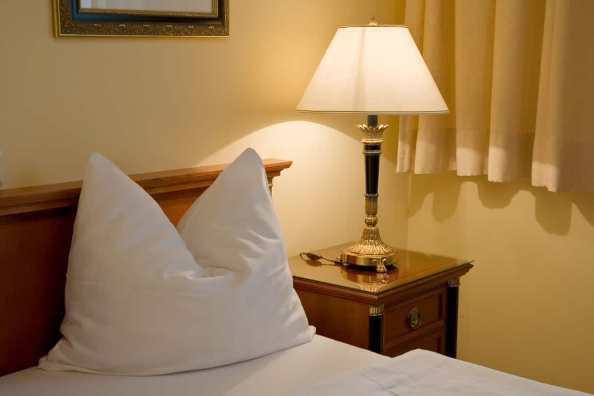 A neatly made bed with two white pillows, a bedside table with a lamp, and a framed picture on the wall.