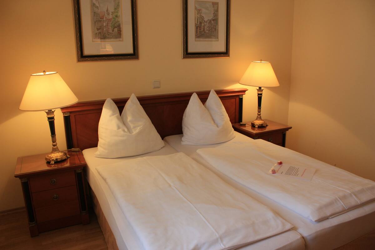 A hotel room with two beds, each with white linens and pillows, two bedside lamps, and two framed pictures on the wall.