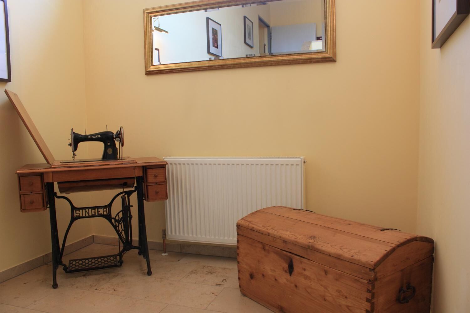 Ein Zimmer mit Nähmaschine, Holzschrank und Heizkörper.