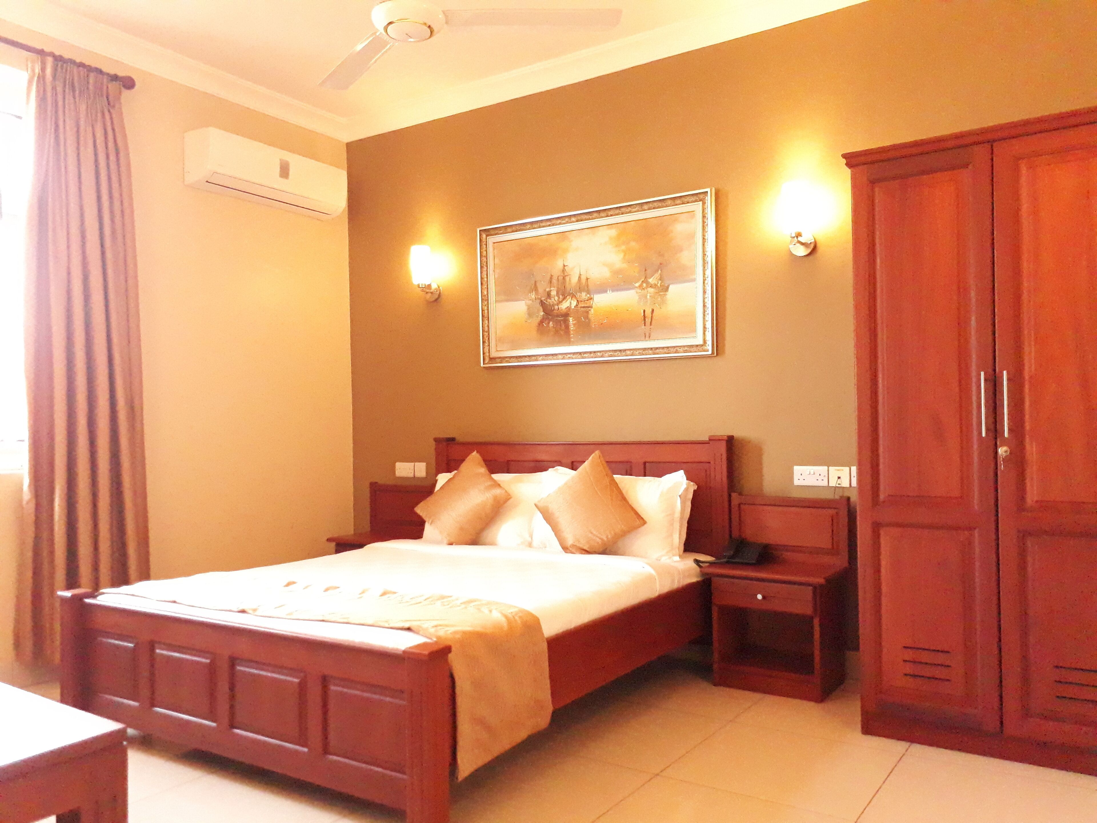 A hotel room with a bed, nightstands, a wardrobe, and a painting on the wall.