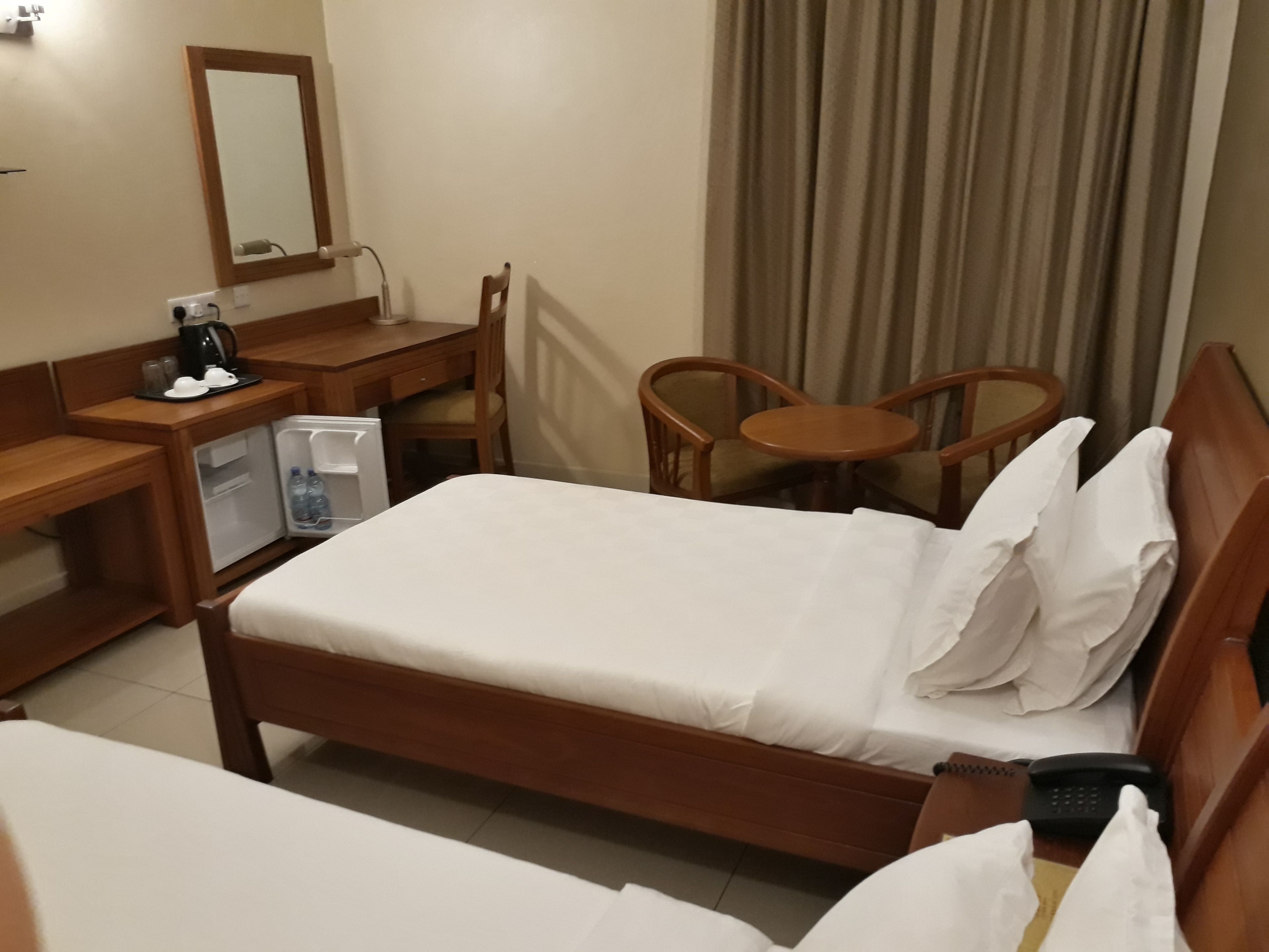 A hotel room with a bed, a desk with a computer, a chair, a small table, and a minibar.