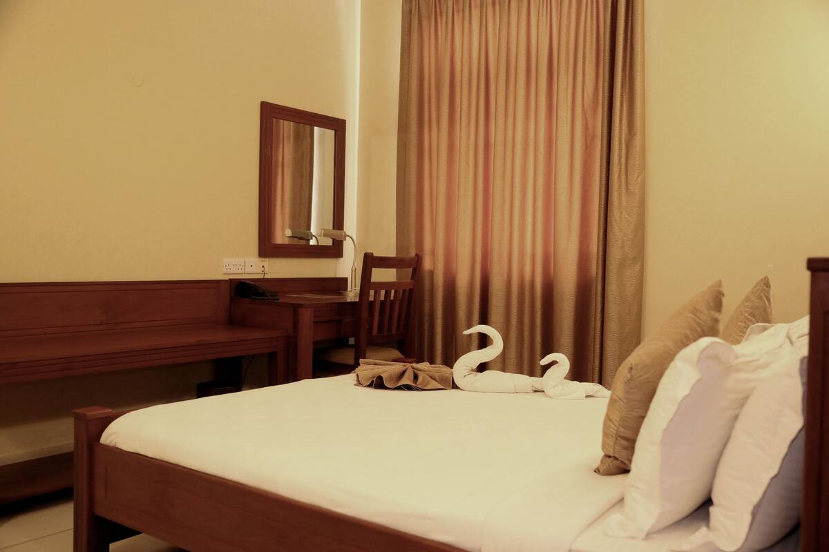 Una habitació d'hotel amb un llit, una taula de fusta, una cadira, un mirall i una cortina.