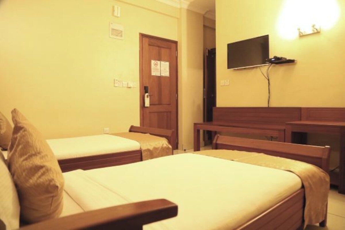 A hotel room with two single beds, a desk, a chair, a TV mounted on the wall, and a door with a sign.