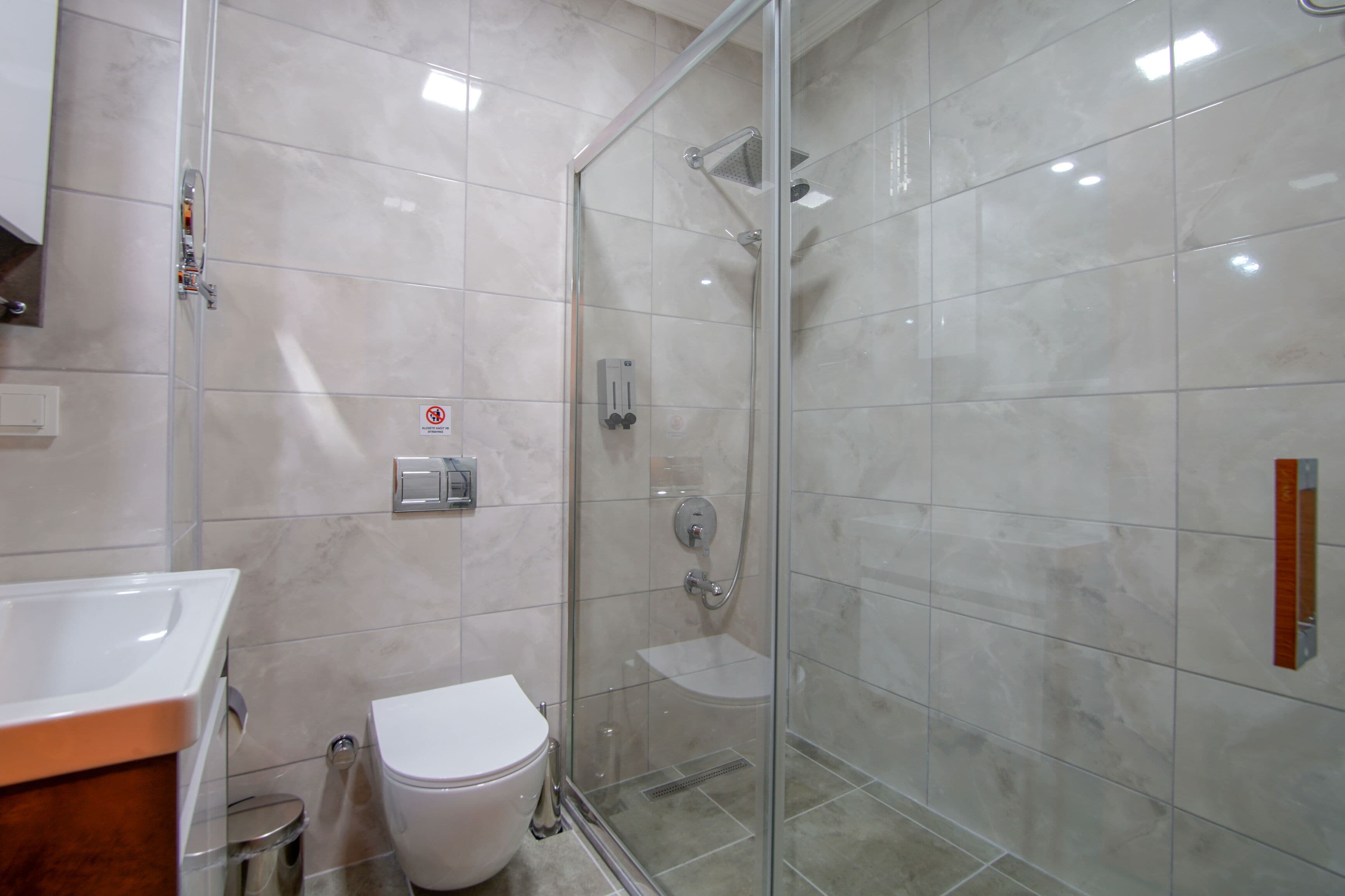 A modern bathroom with a glass-enclosed shower, a white toilet, and a sink with a wooden countertop.