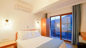 Une chambre à coucher comprenant un lit, des tables de chevet, une armoire et une grande porte-fenêtre coulissante donnant sur un balcon avec vue sur une montagne et un jardin.