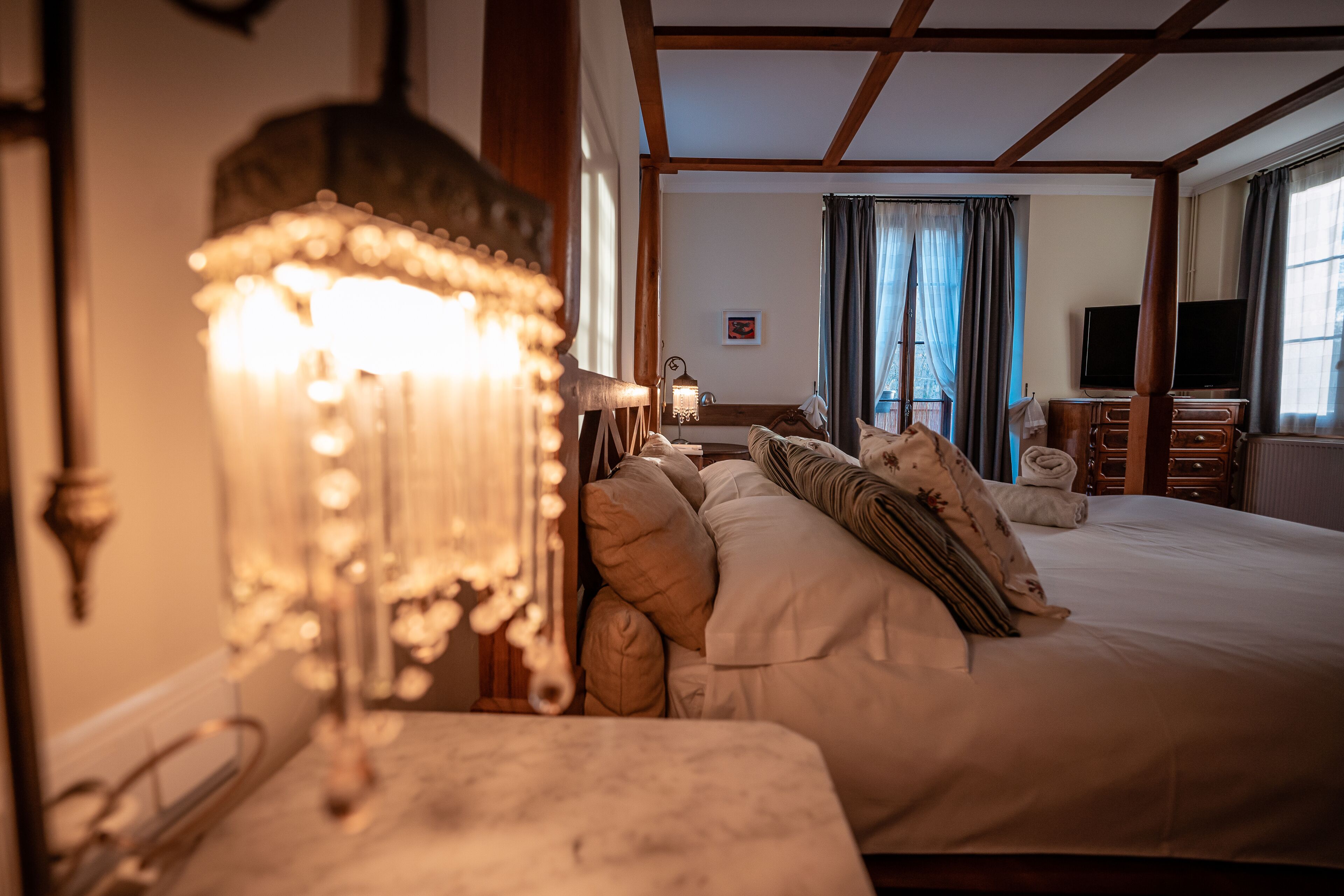 Een goed verlichte slaapkamer met een groot bed, een nachtkastje, een lamp en een televisie in de hoek.