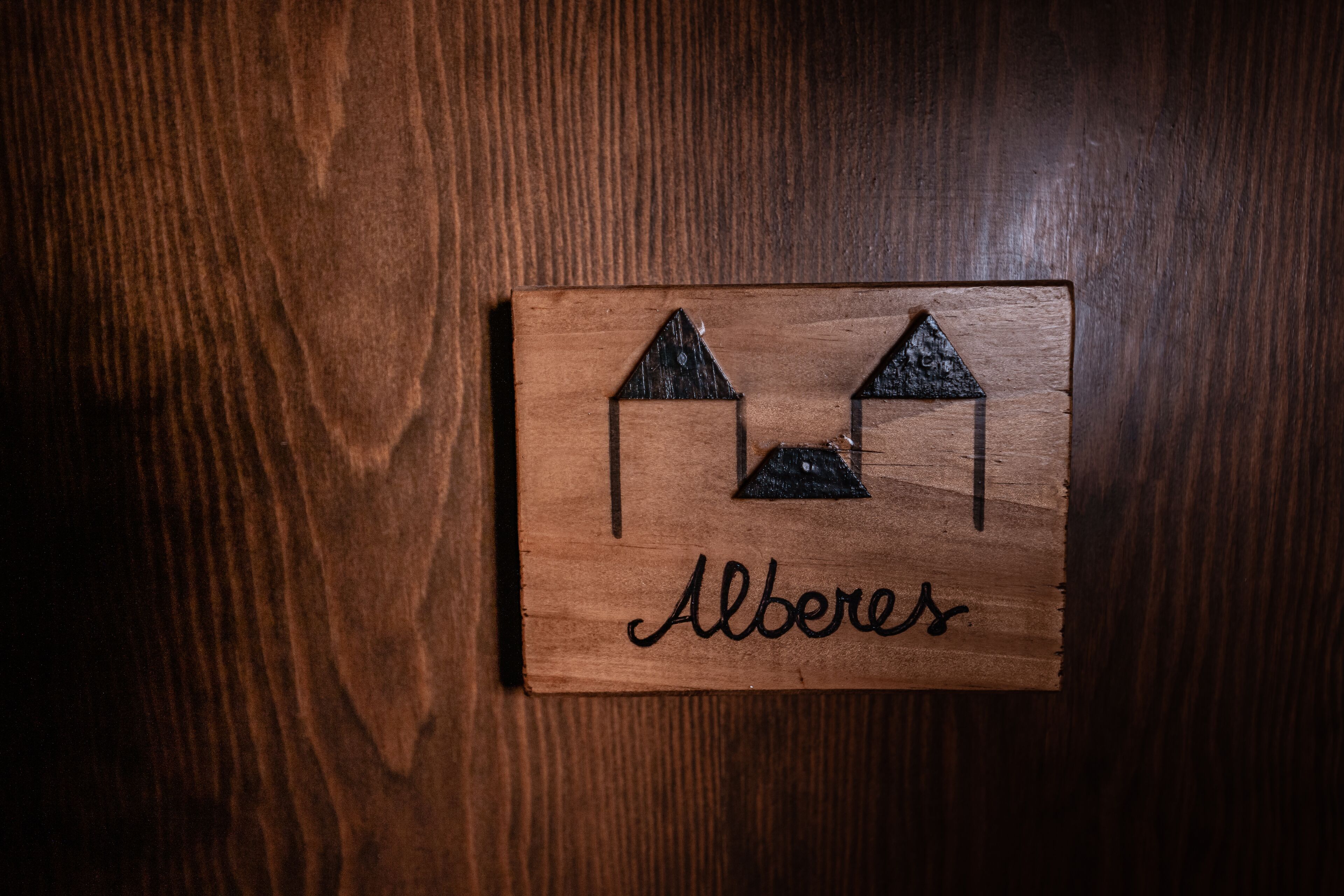 A wooden plaque with a house design and the name "Alberes" on a wooden surface.