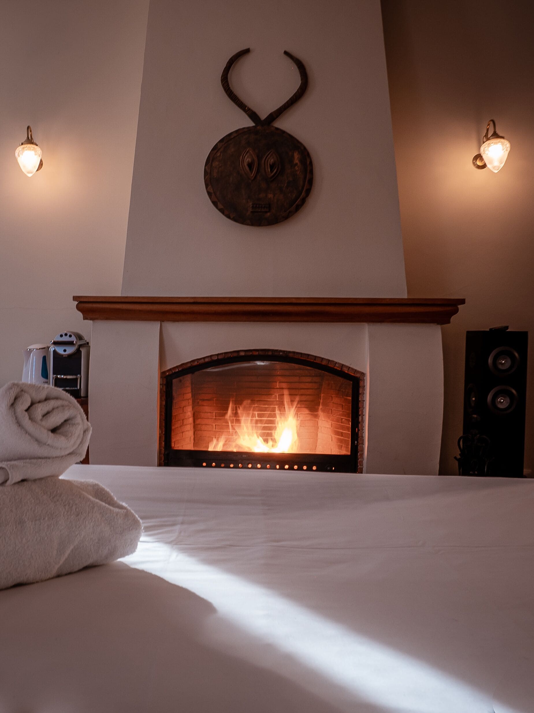 Habitación de hotel con chimenea, una cama con una toalla enrollada e iluminación empotrada.